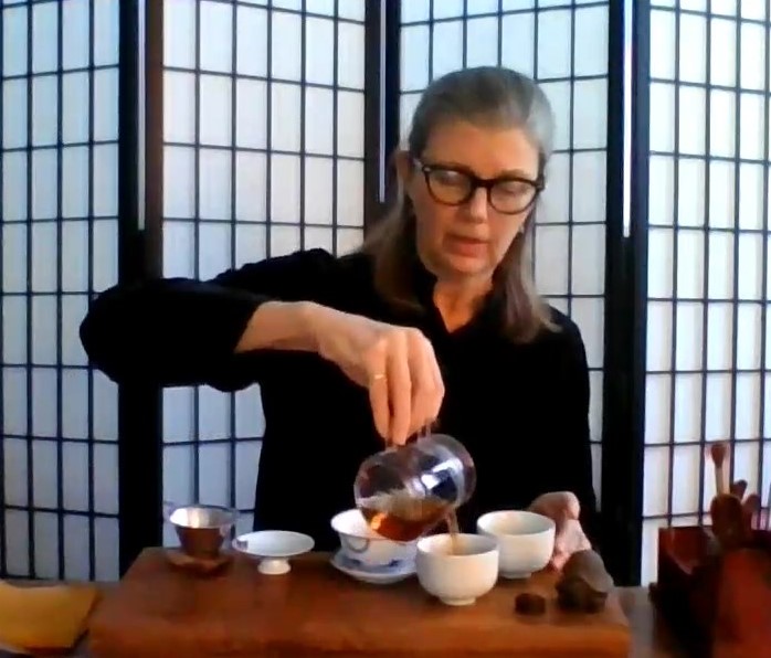 Michelle pouring tea into small white tea cups, set on a tea board in traditional gong fu style.