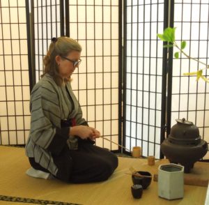 Michelle kneeling in seiza on tatami, holding a hishaku, at the beginning of a Japanese tea ceremony.